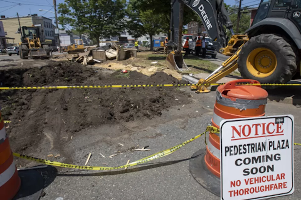 Pedestrian plaza construction site with orange cones and excavator in Jersey City, New Jersey.